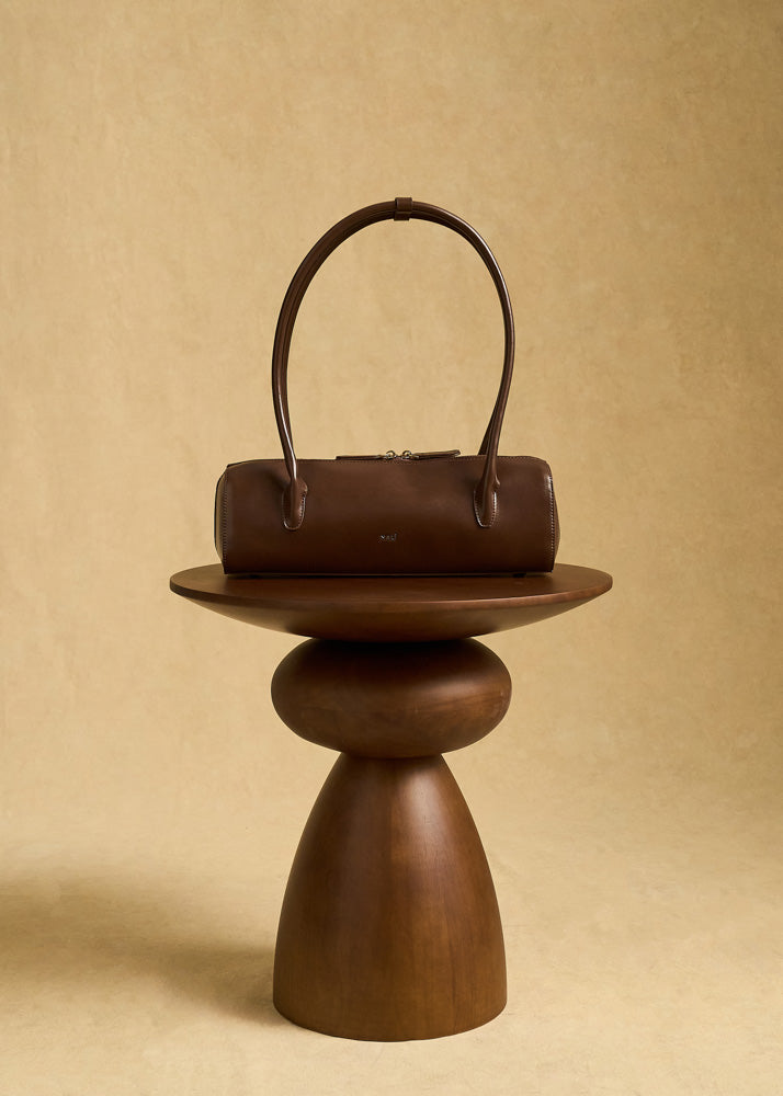 Nalì a spalla billie baguette marrone borsa in pelle marrone scuro con manici curvi appoggiata su base in legno